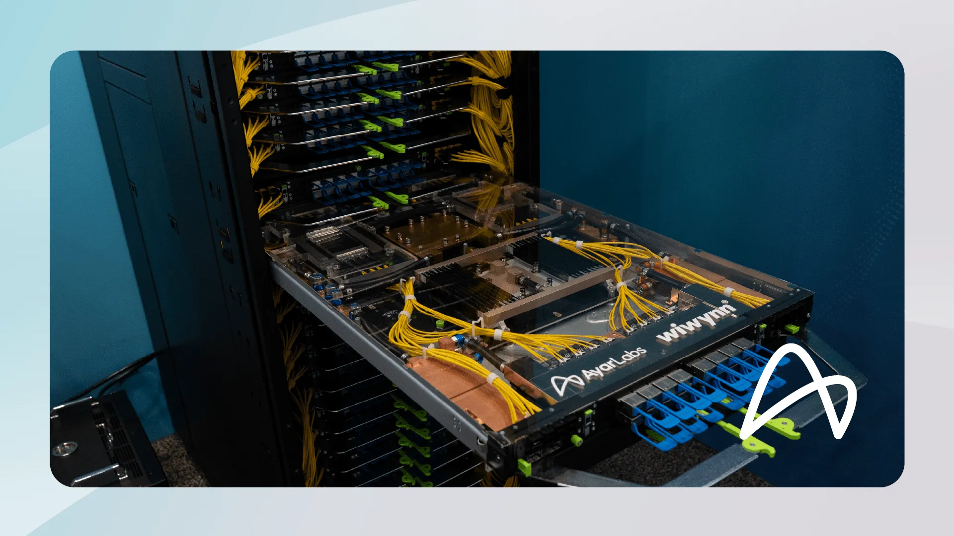 A server tray pulled partway out of a rack, showing yellow optical fibers routed across the board to two processor packages under a clear cover, with Ayar Labs and Wiwynn branding on the front edge.