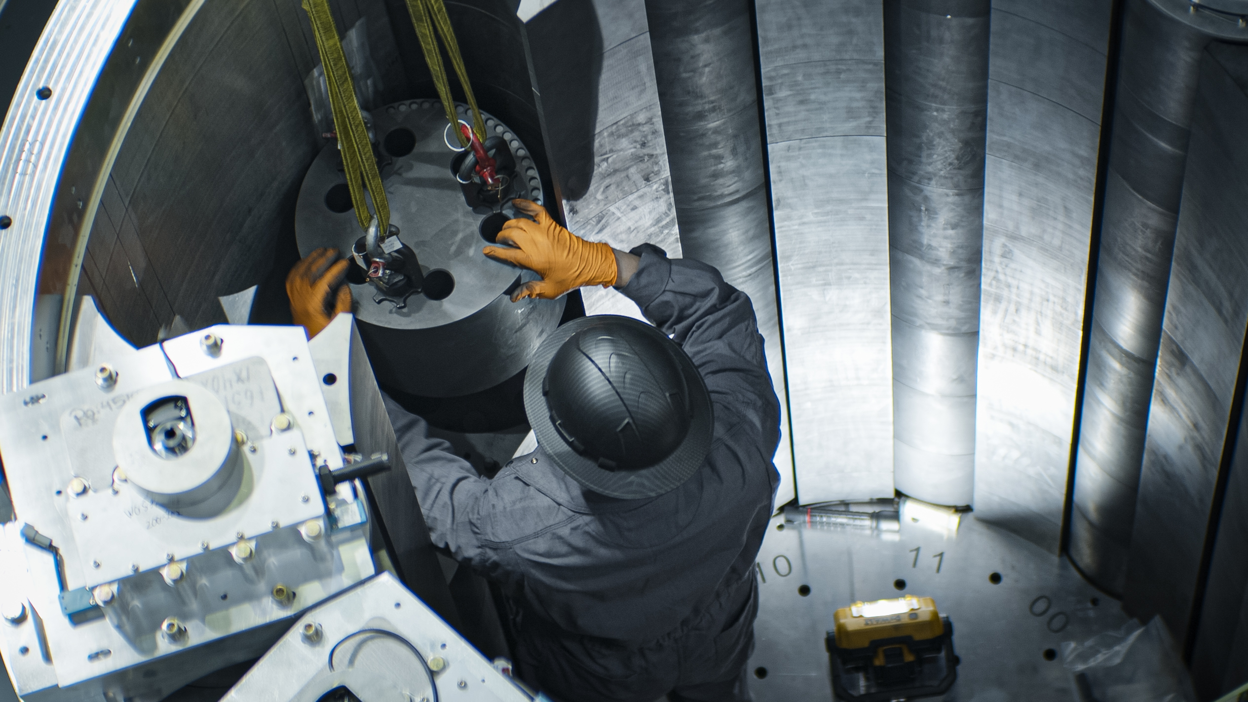 A technician in a hard hat lowers a component into a reactor core assembly, surrounded by graphite blocks and numbered positions.